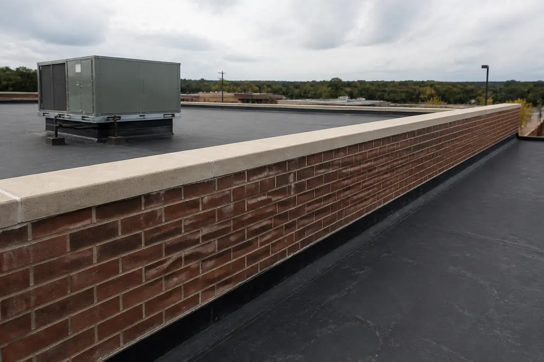 A masonry parapet wall standing above the membrane at the edge of a flat commercial roof
