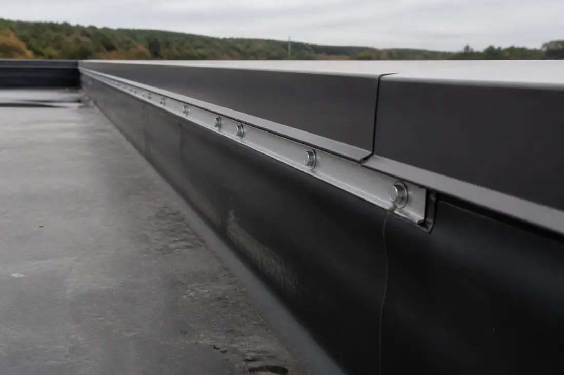 Perimeter edge of a low-slope commercial roof where metal coping meets the membrane